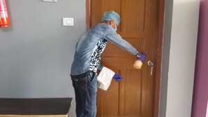 A person in a blue shirt and jeans opening a wooden door with a key. - Hotel Greenwood (Siliguri)