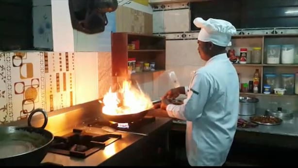 A chef cooking with a large flame in a kitchen. - Hotel Greenwood (Siliguri)