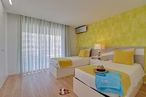 Ein Hotelzimmer mit zwei Betten, einem großen Fenster mit Vorhängen, einem Flachbildfernseher und einer gelben Akzentwand.