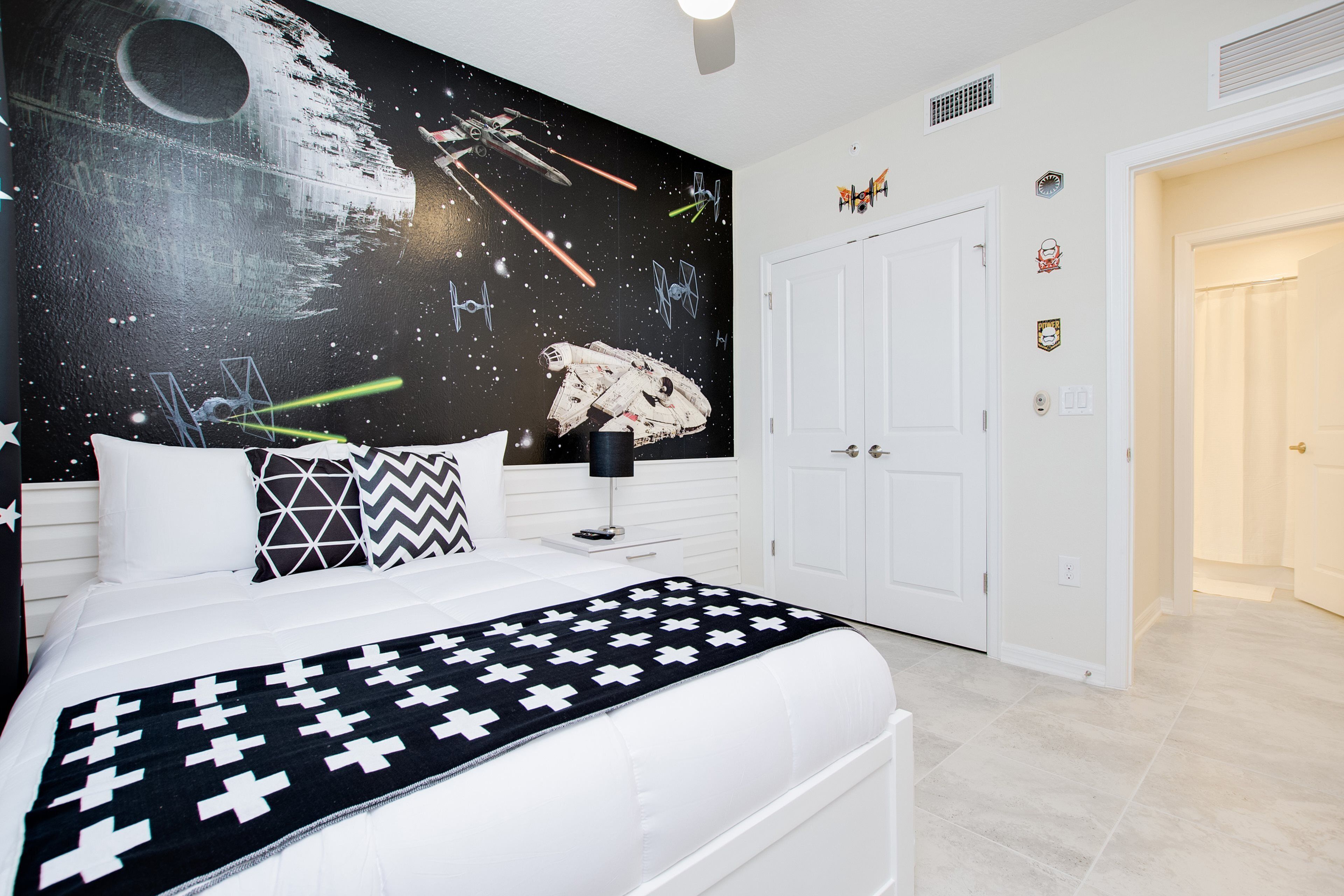 A bedroom with a Star Wars-themed wall mural, a white bed, and a cross-patterned blanket.