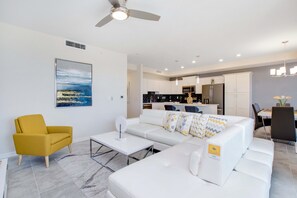 A modern living room with a white sofa, a yellow armchair, and a dining area with a table and chairs.