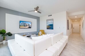 A modern living room with a white sofa, a ceiling fan, a flat-screen TV mounted on the wall, and a potted plant. - 3120paraunit306 (Kissimmee)