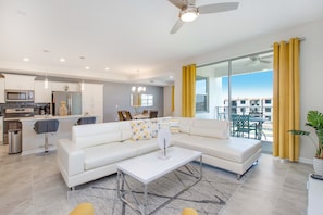 A modern living room with a white sectional sofa, a coffee table, and a dining area with a glass top table and chairs. - 3120paraunit306 (Kissimmee)