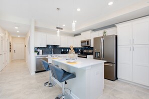 A modern kitchen with white cabinets, stainless steel appliances, and a central island with bar stools.