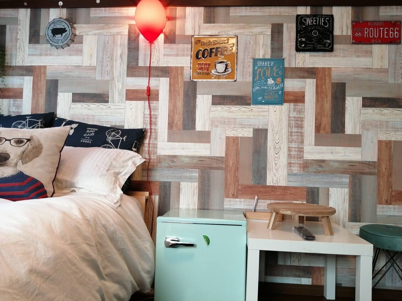 A bedroom with a bed, a small table, a nightstand, and a wall with various signs and a wooden pattern.