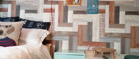 A bedroom with a bed, a small table, a nightstand, and a wall with various signs and a wooden pattern.