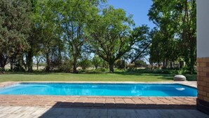 A swimming pool with a brick deck, surrounded by trees and a grassy lawn. - Gannabos Guest House (Gariep)