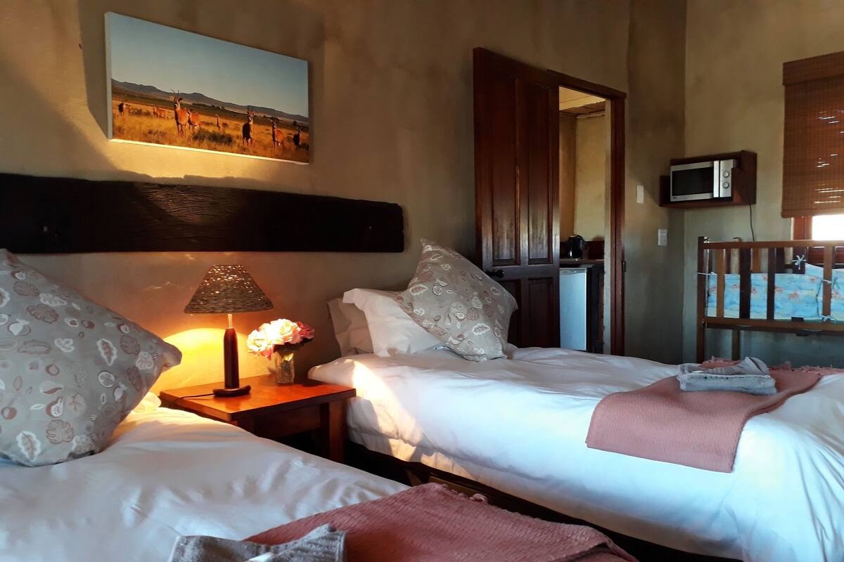 A hotel room with two beds, a bedside table with a lamp, a painting on the wall, a wooden headboard, and a television on a stand.