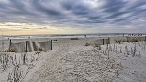 Una spiaggia con una recinzione di legno, dune sabbiose e l'oceano sullo sfondo.
