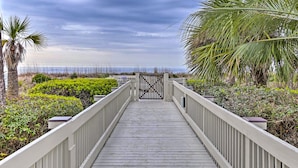 Una passerella in legno conduce a un cancello con vista sulla spiaggia e sull'oceano.