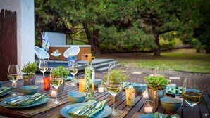 An outdoor dining area with a wooden table set for a meal, surrounded by greenery.