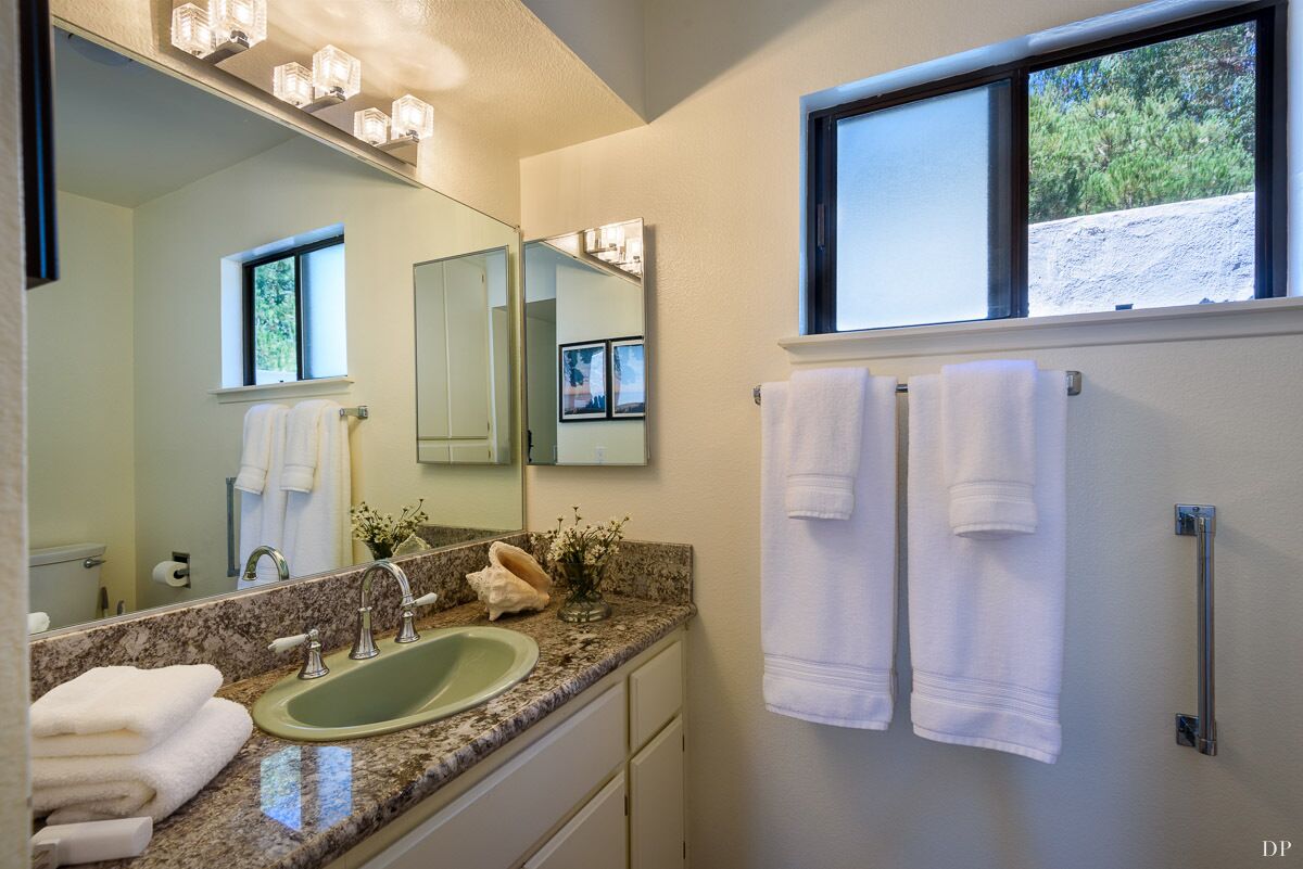 A bathroom with a granite countertop, a sink, a mirror, and a window.