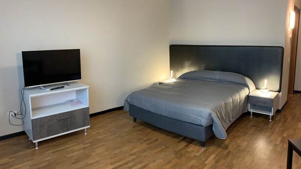 A bedroom with a bed, bedside tables with lamps, a TV on a stand, and a wooden floor.