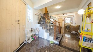 A spacious living area with a wooden door, a staircase with a wooden railing, and a yellow shoe rack. - J&J B&B (Hengchun)