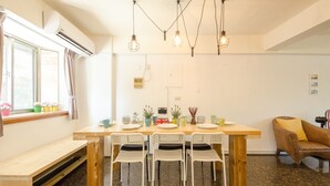 A dining area with a wooden table, white chairs, and hanging light fixtures. - J&J B&B (Hengchun)
