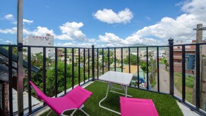 A balcony with a small table and two pink chairs, overlooking a residential area with buildings and a road. - J&J B&B (Hengchun)