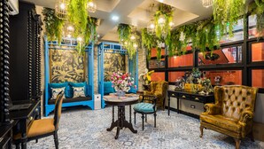 Una habitación con un sofá azul, una mesa redonda con un florero, un sillón amarillo y plantas colgantes.