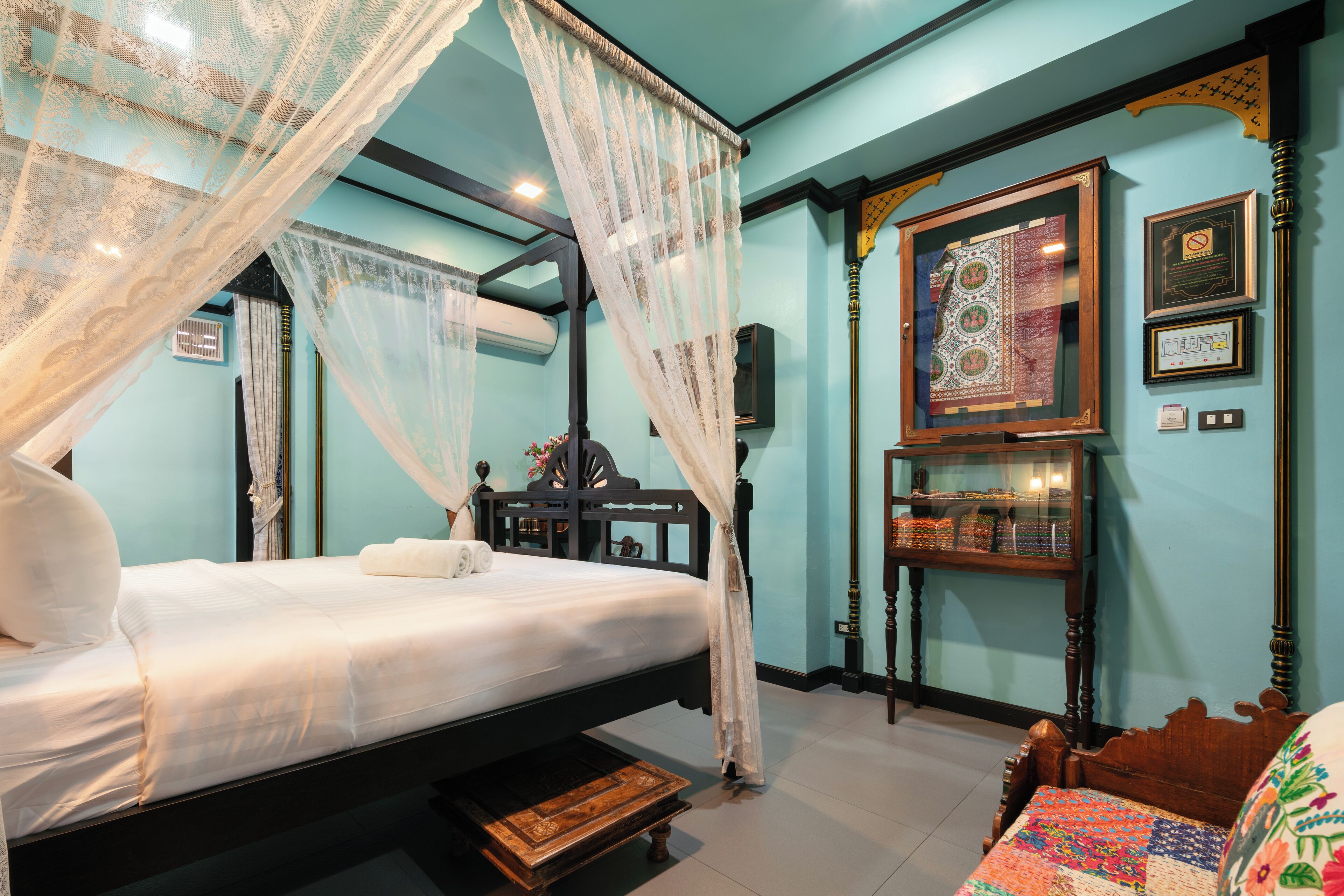 A four-poster bed with a canopy, a wooden nightstand, a wall-mounted shelf with decorative items, and a framed tapestry.