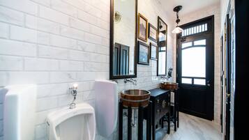 Et moderne badeværelse med hvide, rektangulære fliser, et sort toiletbord med trædetaljer, et hvidt pissoir og et stort spejl.
