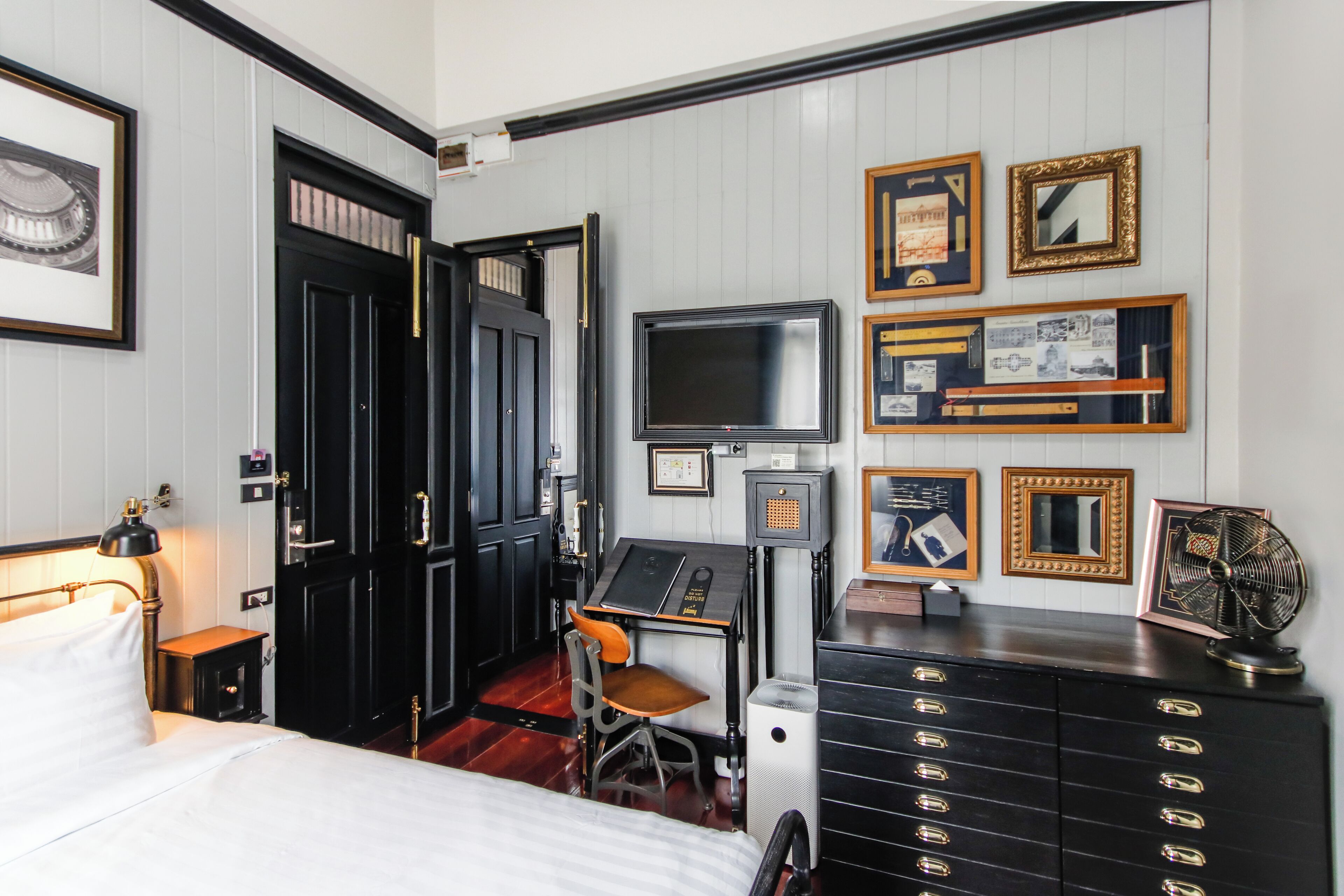 A hotel room with a bed, desk, chair, TV, dresser, and wall-mounted artwork.