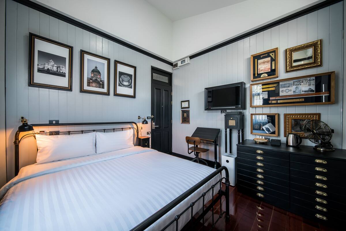 Un dormitorio ordenado con cama, cómoda, escritorio y televisor en la pared.