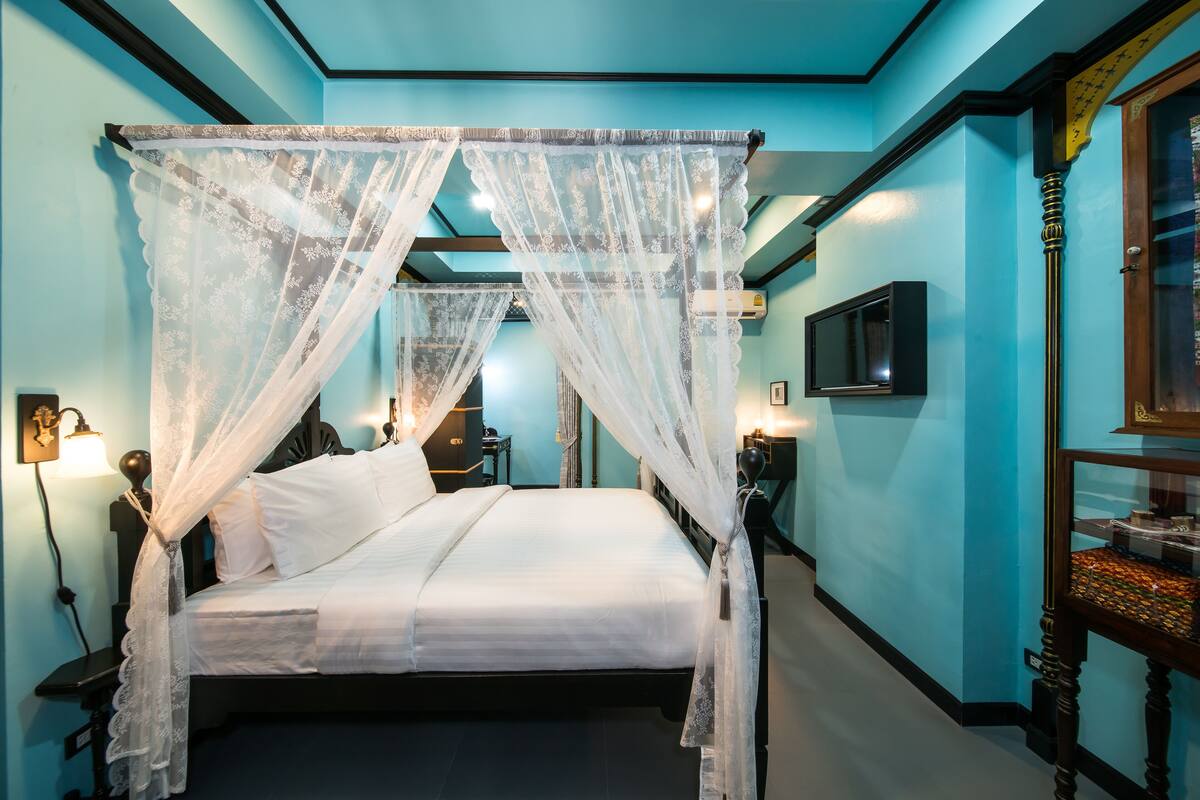 Una cama con dosel, un televisor de pantalla plana en la pared y una mesita de noche con lámpara.
