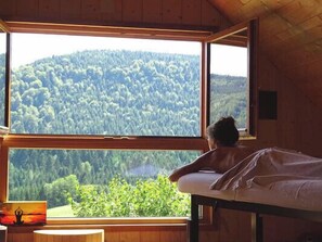 Ein Zimmer mit großem Fenster mit Blick auf einen bewaldeten Hang.