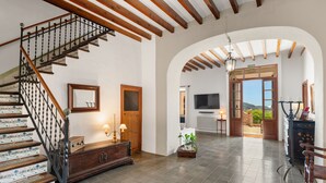 A spacious interior with a wooden staircase, a large arched doorway, a television, and a view of the outdoors. - 44066 Finca Biniforani Nou (Buñola)