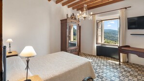 A bedroom with a bed, a dresser, a chandelier, a TV, and a window with a view. - 44066 Finca Biniforani Nou (Buñola)