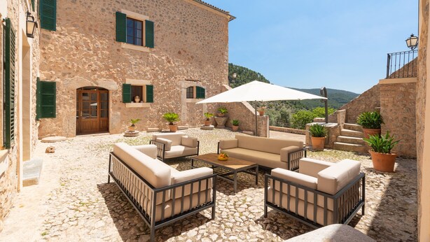 A stone building with a courtyard featuring outdoor furniture, potted plants, and a large umbrella. - 44066 Finca Biniforani Nou (Buñola)