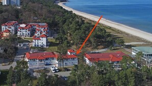 Un quartier résidentiel situé sur la côte, avec une plage, des maisons aux toits rouges et un grand bâtiment surmonté d’un toit végétalisé.