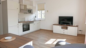 Une cuisine moderne avec des meubles blancs, un four à micro-ondes et un grand téléviseur posé sur un meuble en bois.