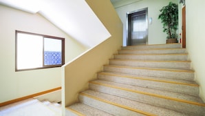 A staircase with a handrail, a window with a blue grid pattern, and a potted plant. - OYO 917 PK Residence Pattaya (Pattaya)