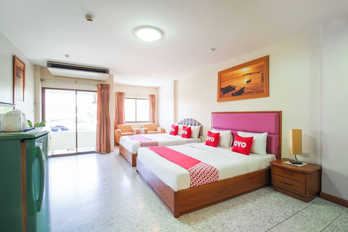 Una habitació d'hotel amb dos llits, una finestra gran, un aire condicionat, una tauleta de nit i un quadre a la paret.