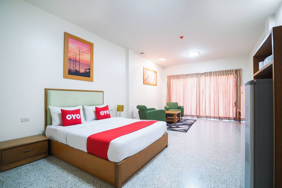 Habitació d'hotel amb un llit gran, dues cadires, una taula petita i vista a l'exterior a través d'una finestra amb cortines.
