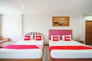 Une chambre d’hôtel avec deux lits, chacun agrémenté d’un oreiller rouge à l’effigie de la marque OYO, d’une tête de lit en bois et d’un tableau au-dessus des lits.
