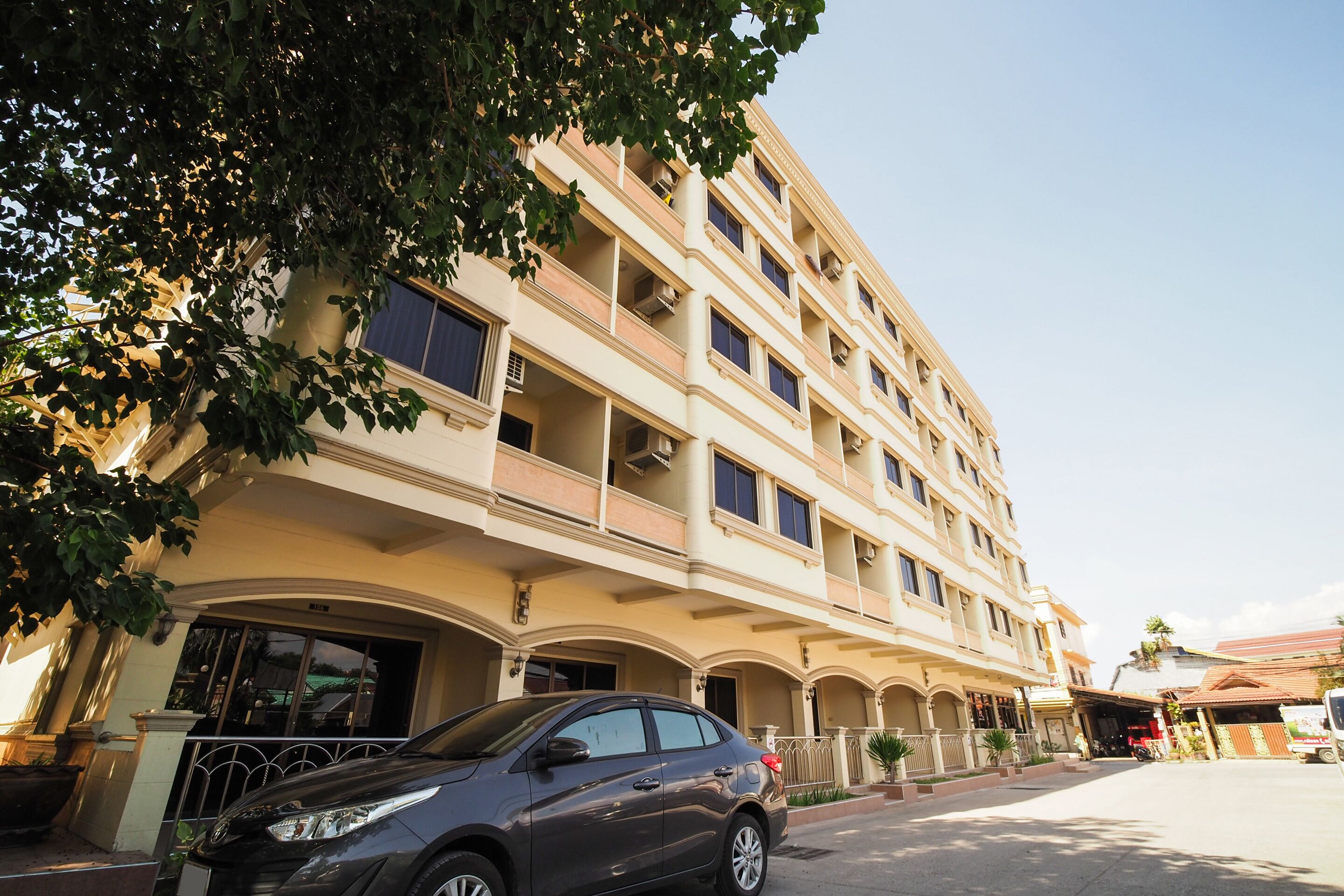 A multi-story hotel with balconies, a car parked in front, and a clear sky.