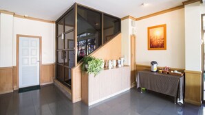 A reception area with a wooden reception desk, a glass partition, a potted plant, a framed picture, and a coffee station. - OYO 917 PK Residence Pattaya (Pattaya)