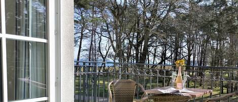 A balcony with wicker chairs and a table, overlooking a forested area.