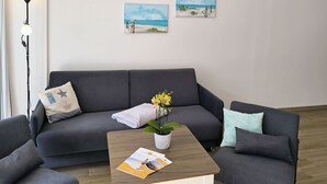 Ein modernes Wohnzimmer mit einem grauen Sofa, einem Couchtisch mit einer Zeitschrift und einer Zimmerpflanze.