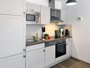 A modern kitchen with white cabinetry, a built-in microwave, a stove, and a coffee maker.