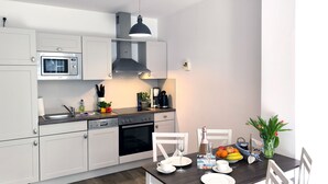 Eine moderne Küche mit weißen Schränken, einem eingebauten Ofen und einem Essbereich mit einem Holztisch und weißen Stühlen.