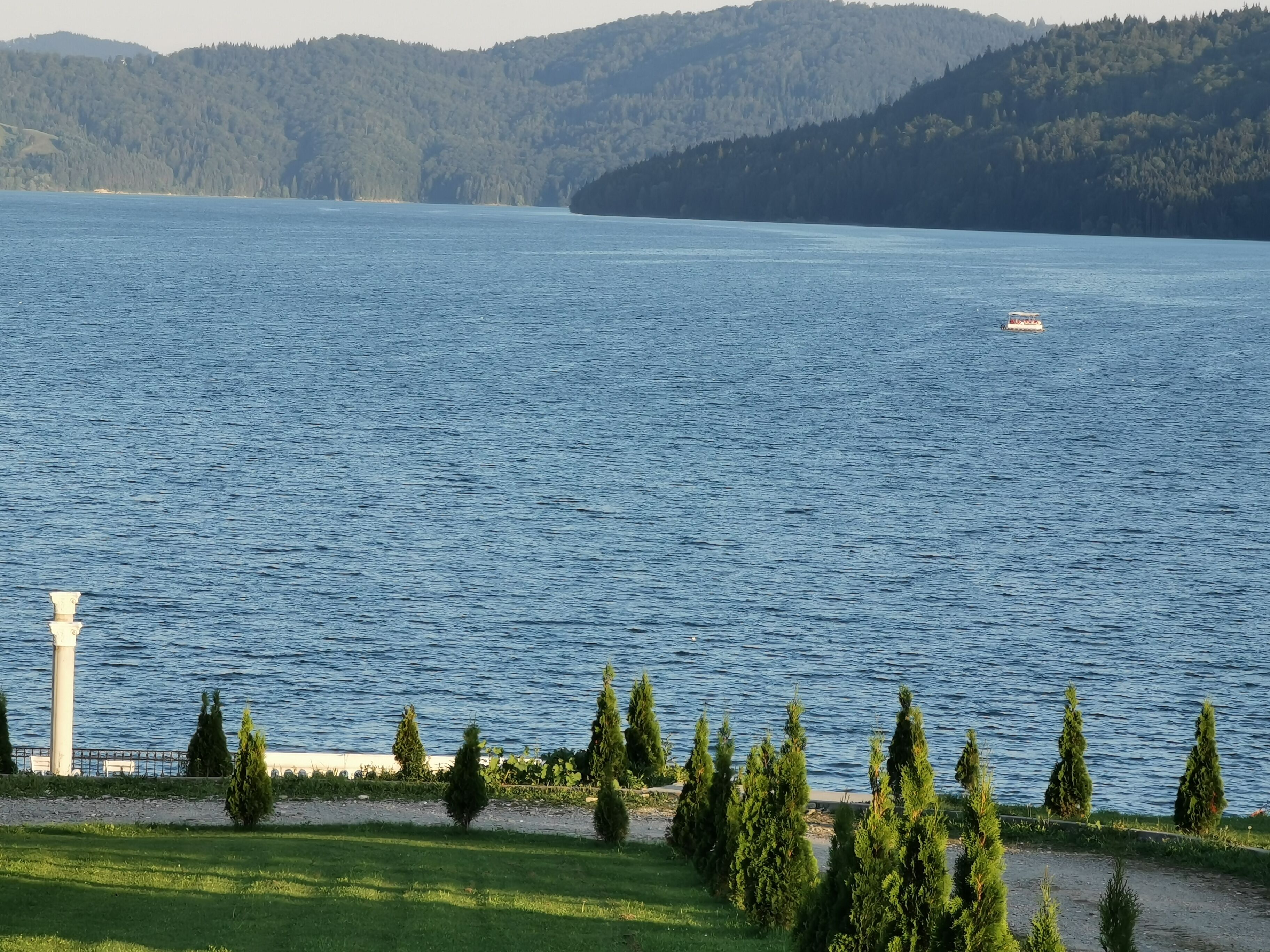 A lake with a boat, surrounded by trees and hills.