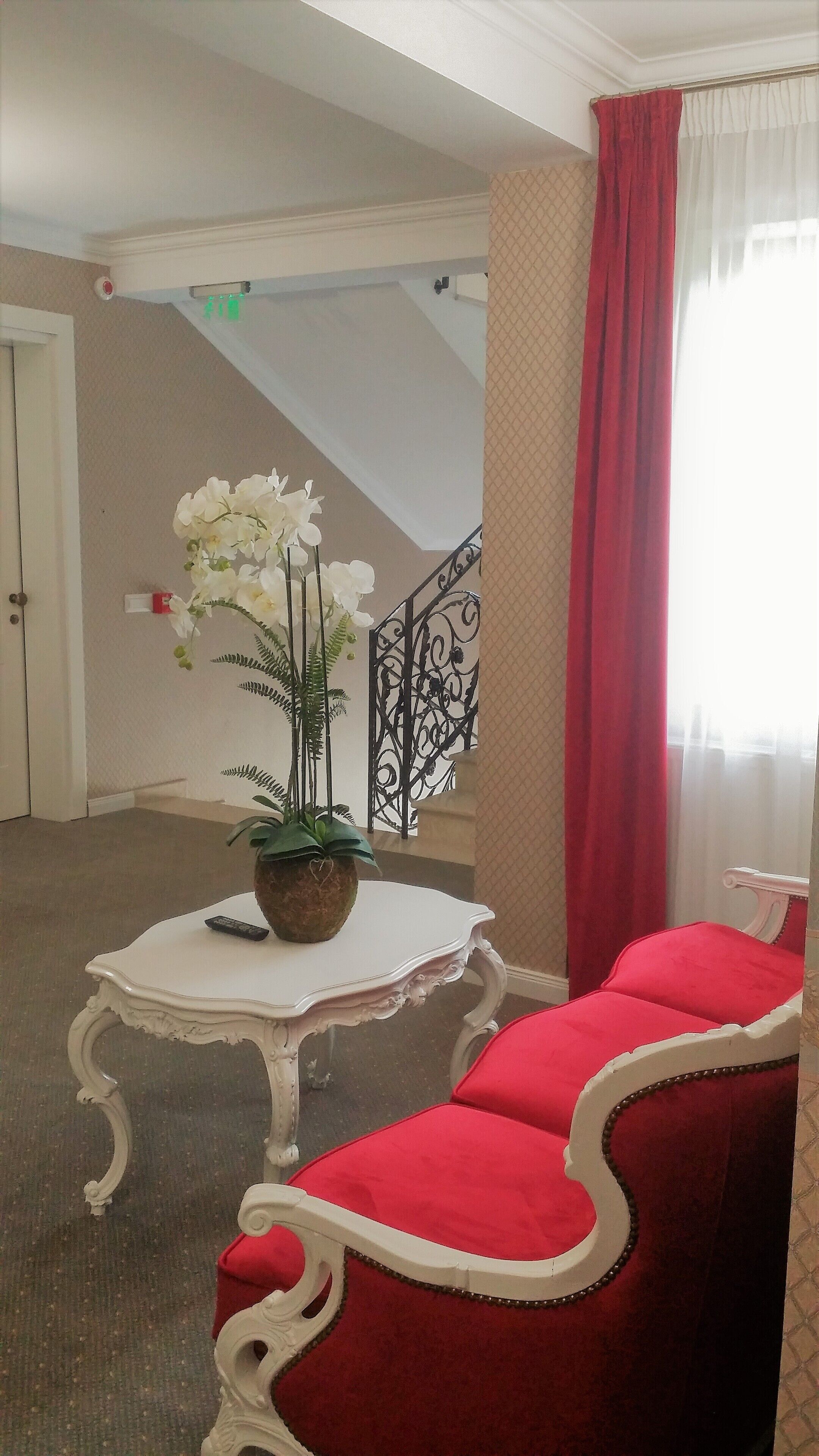Hotelkamer met een witte tafel, rode stoelen, een potplant en een trap op de achtergrond.