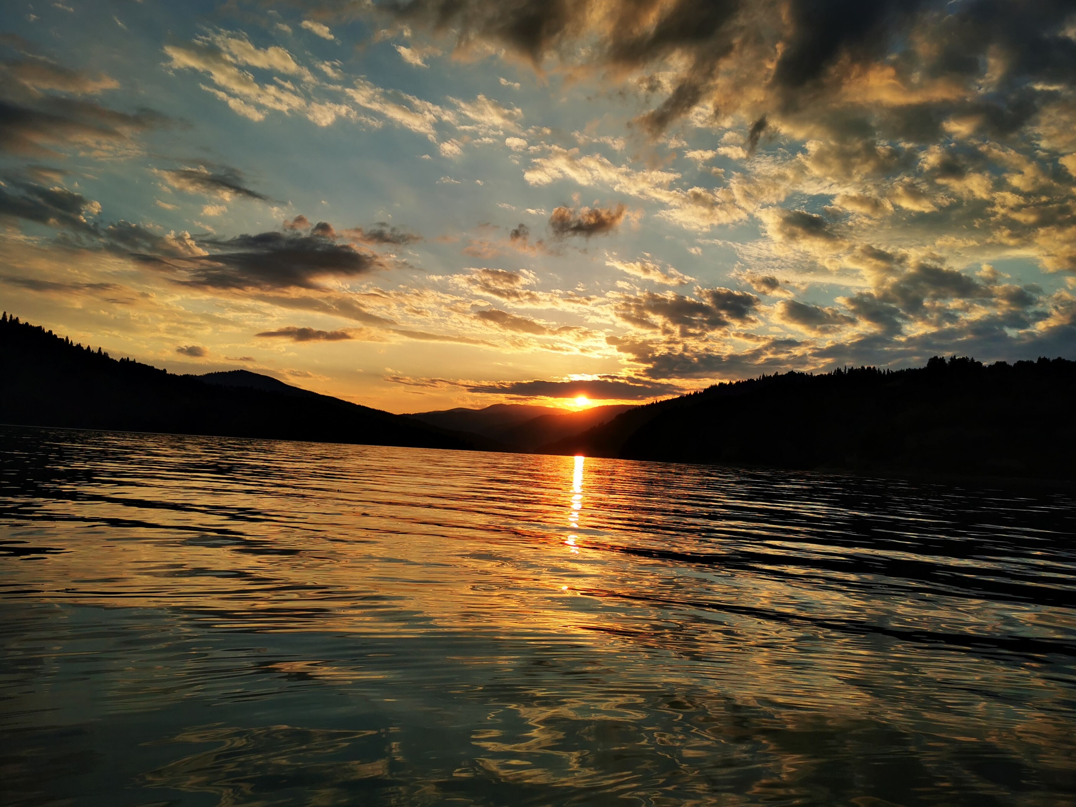 Ein Sonnenuntergang über einem ruhigen See, im Hintergrund Berge.