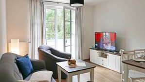 Un salon avec un canapé, un fauteuil et un téléviseur posé sur un meuble blanc.