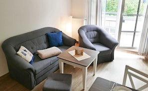 Un salon moderne avec un canapé gris, un fauteuil gris, une petite table en bois et une table basse en verre.