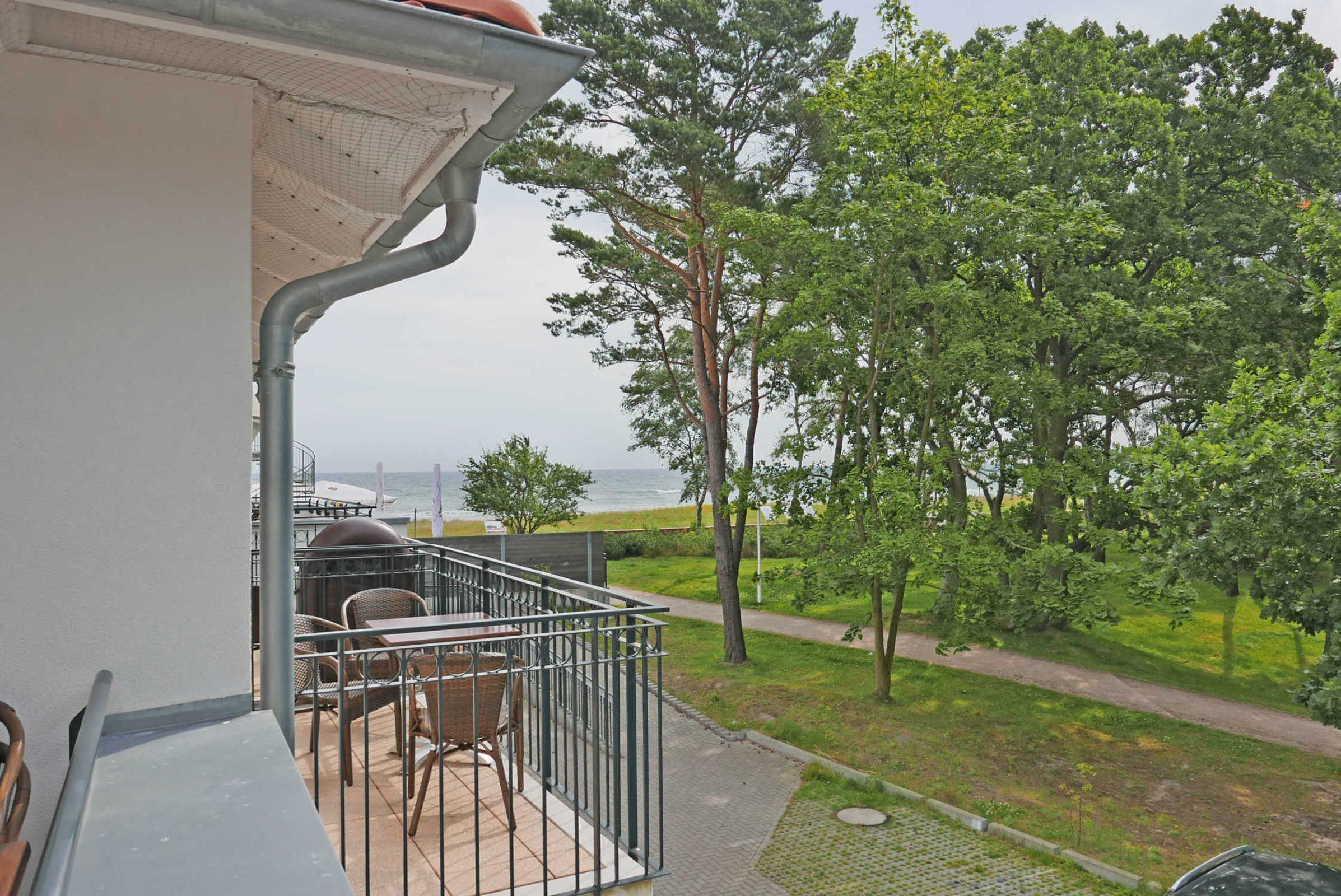 A balcony with outdoor seating, a view of the sea, and a pathway leading to a grassy area.