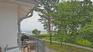 Un balcon avec des sièges pour l’extérieur, une vue sur la mer et un chemin menant à une zone herbeuse.
