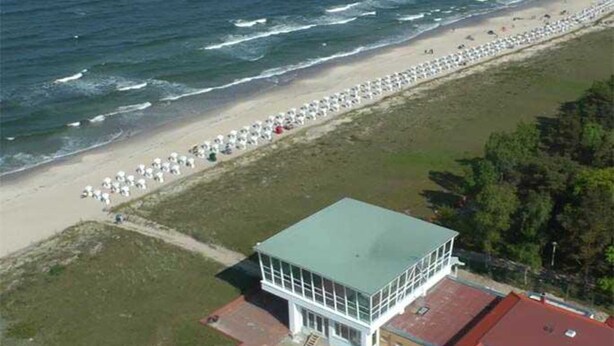Vue aérienne d’une plage, avec une rangée de parasols et un bâtiment doté d’un toit végétalisé.